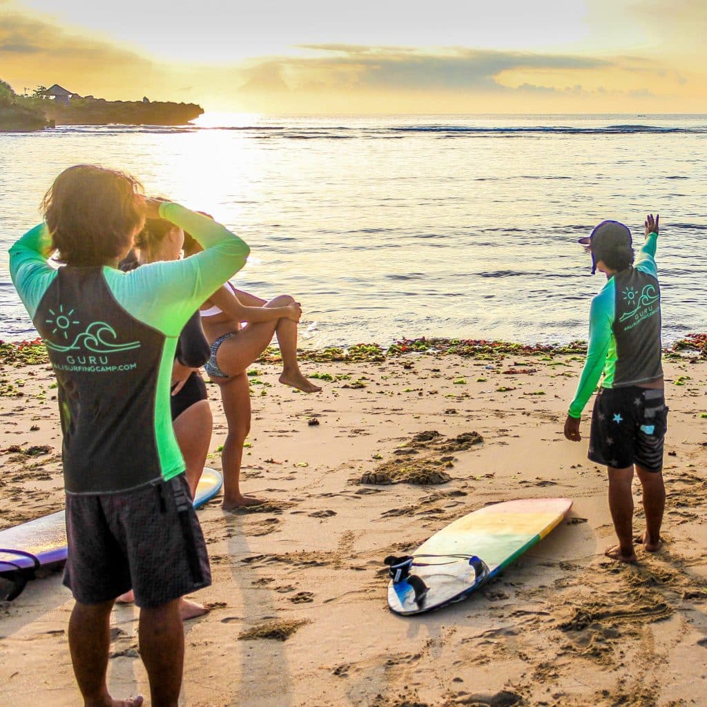 Surfers standing on the beach at sunrise.